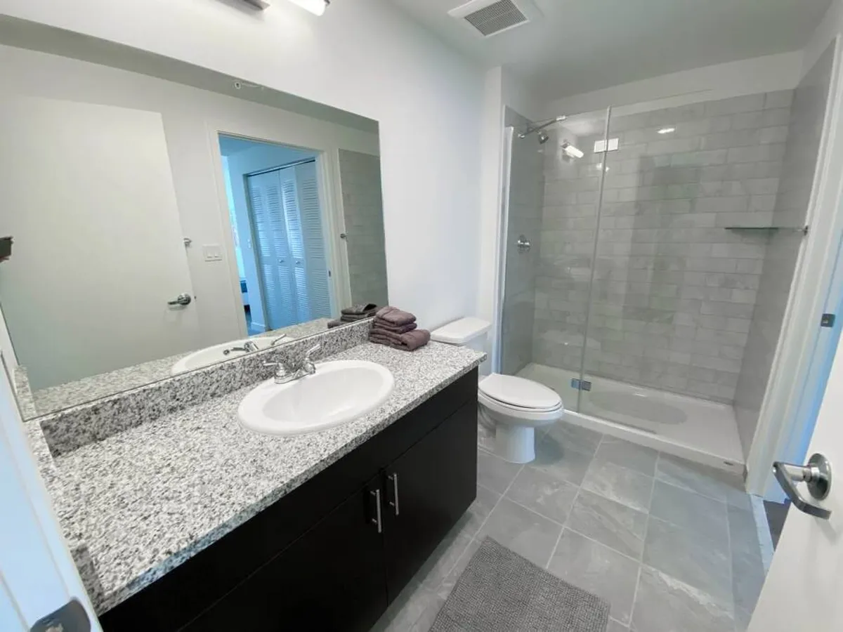 A modern bathroom with a granite countertop, large mirror, glass-enclosed shower, and toilet. The space exudes freshness and cleanliness, essential for long-term comfort and convenience.